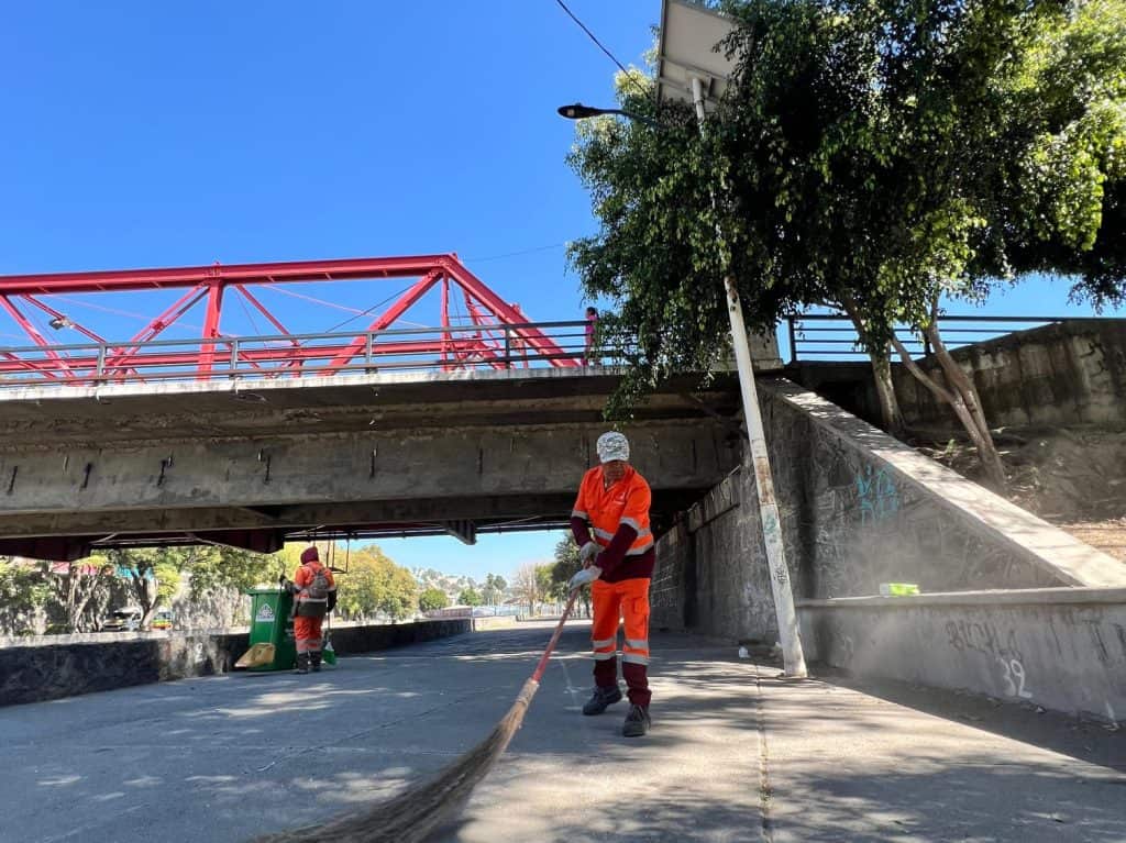 1. Obreros limpian debajo de un puente en Tlaxcala, México, en un día soleado, con cielo despejado y árboles verdes, para mantener la limpieza urbana.
