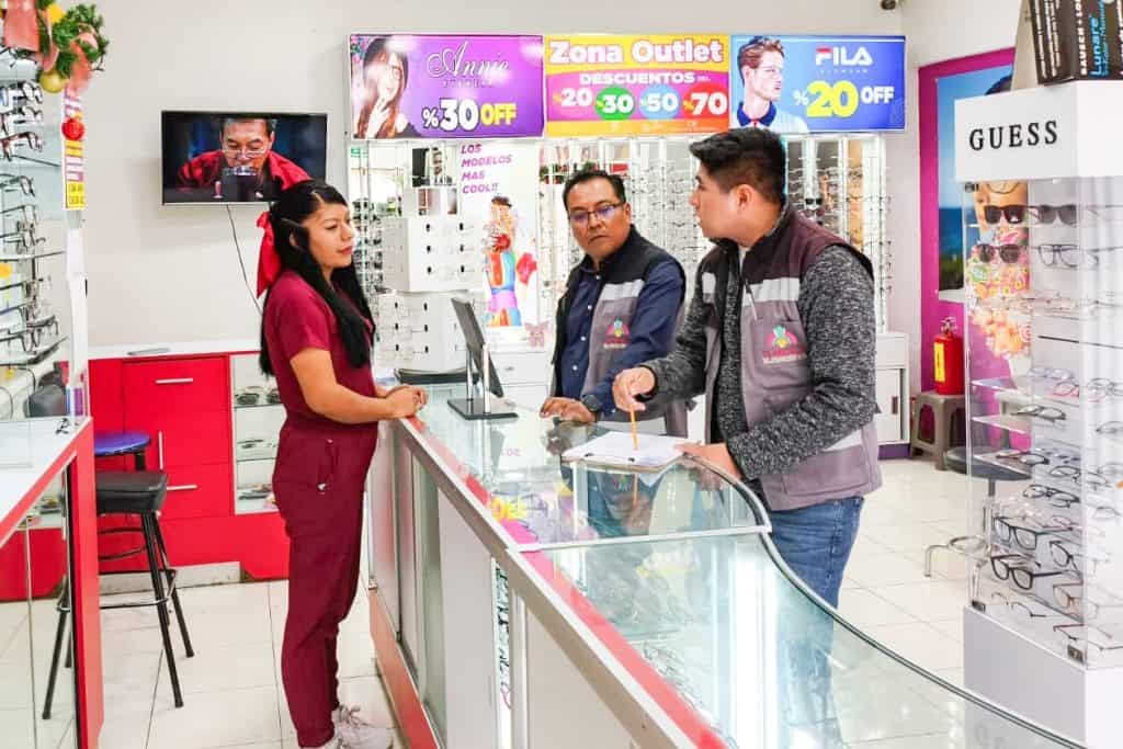 Compra y atención en tienda de ópticas con dos empleados y cliente en Tlaxcala, destacando promociones en lentes y accesorios, en un entorno comercial moderno y bien iluminado.
