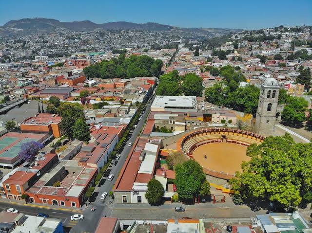 1. Imagen aérea de Tlaxcala mostrando la ciudad, calles, árboles y la plaza principal con su tradicional ronda, montada en una zona central rodeada de edificios y áreas verdes.