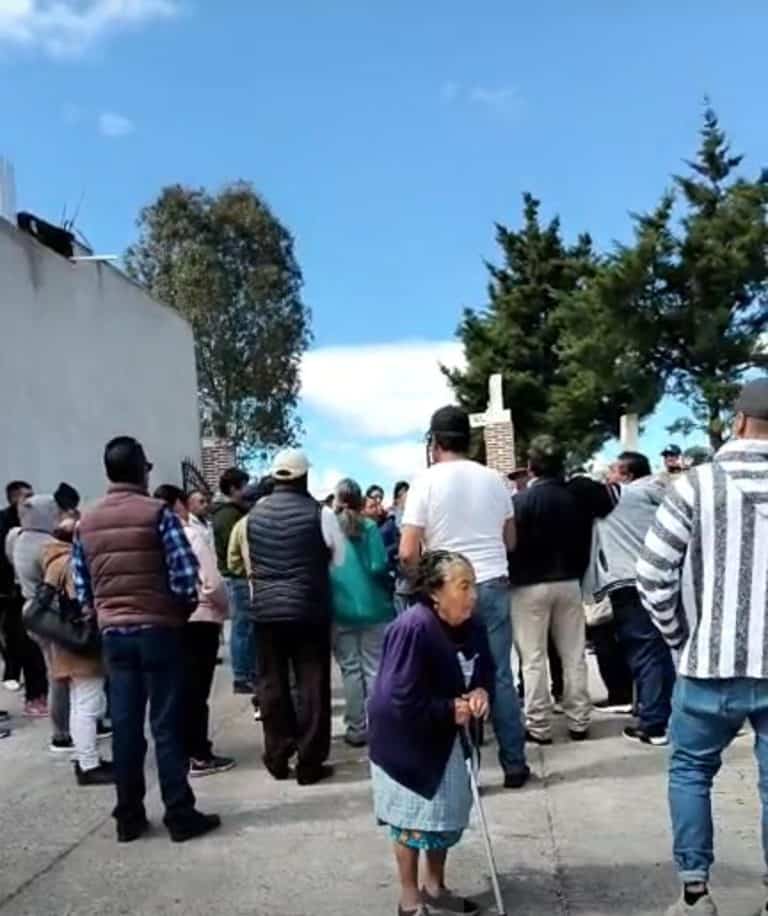 1. Personas reunidas en una ceremonia al aire libre en Tlaxcala, con cielo azul y árboles en el fondo, participando en un evento comunitario.