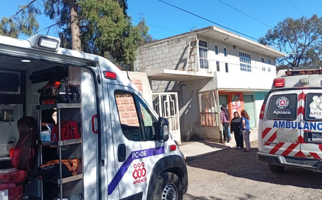 Atención de paramédicos y familiares en la entrada de una vivienda en Tlaxcala tras un incidente, con ambulancias del municipio presente.