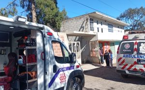 Atención de paramédicos y familiares en la entrada de una vivienda en Tlaxcala tras un incidente, con ambulancias del municipio presente.