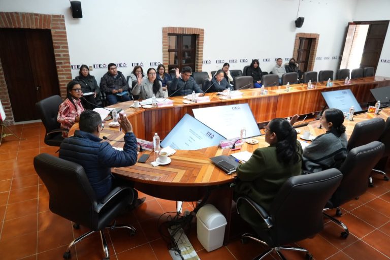 1. Mujeres y hombres en una junta en un salón con mesas de madera, participando en una votación o discusión importante.