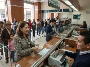 1. Personas realizando trámites en ventanillas de un banco con fila de clientes esperando su turno.