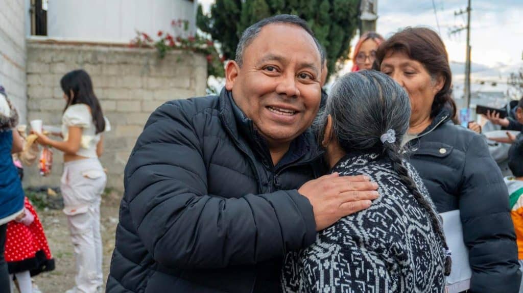1. Hombre sonriendo y abrazando a una mujer mayor en un evento social al aire libre, rodeado de personas y niños.