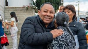 1. Hombre sonriendo y abrazando a una mujer mayor en un evento social al aire libre, rodeado de personas y niños.