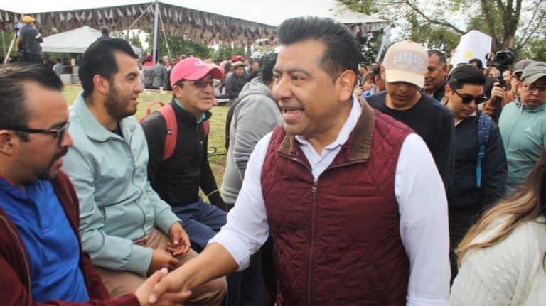 1. Hombre saludando a un grupo de personas en un evento al aire libre en Tlaxcala, México, con ambiente festivo y diversas actividades presentes.