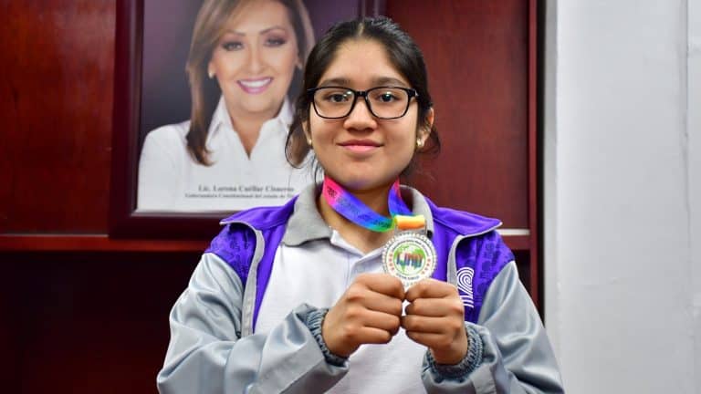 1. Niña con medalla de competencia de ciencia y tecnología, usando gafas y mochila, en interior con retrato de una mujer en el fondo.
