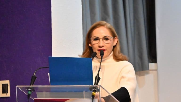 1. Mujer con gafas y peinado elegante hablando en conferencia con micrófonos y portátil, en un evento formal.