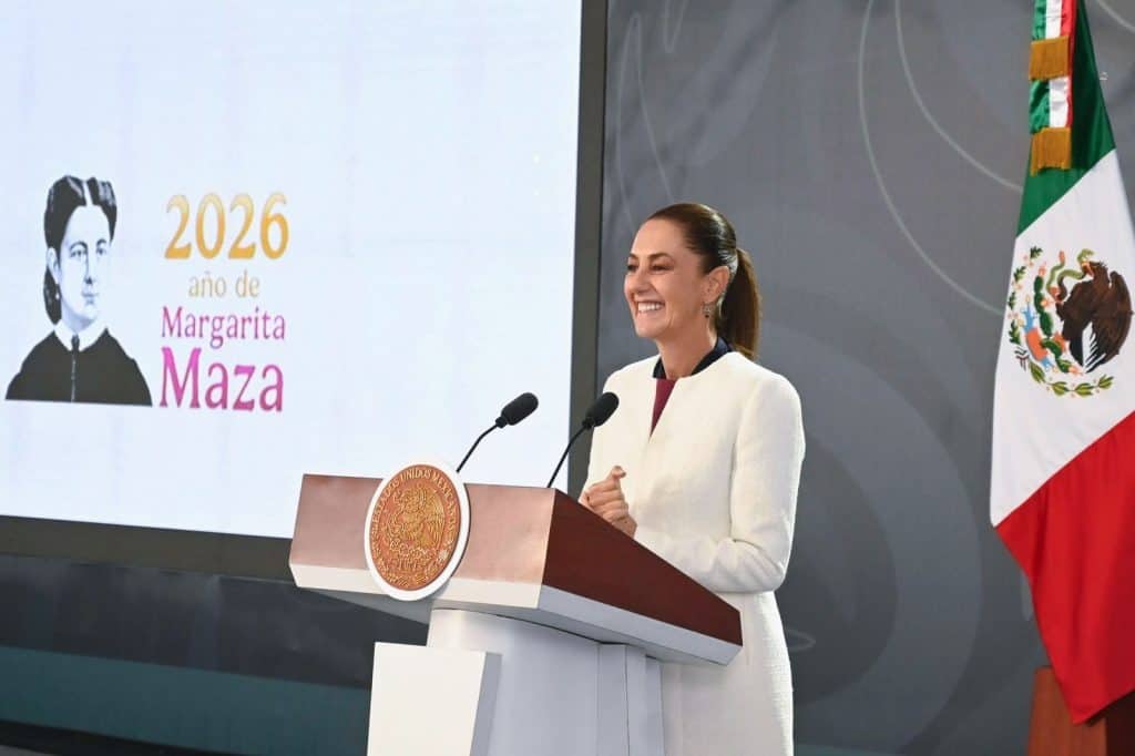 1. Mujer sonriente en podio con bandera de México y pantalla que dice "2026 año de Margarita Maza".