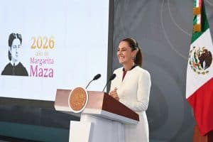 1. Mujer sonriente en podio con bandera de México y pantalla que dice "2026 año de Margarita Maza".