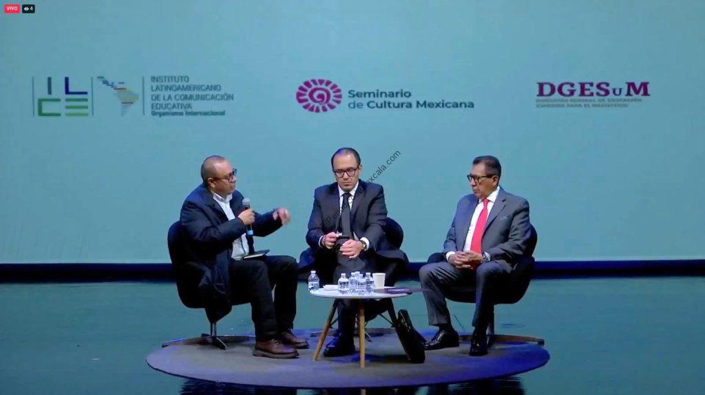 La imagen muestra a tres hombres en un panel de discusión en un escenario con fondo azul y logotipos institucionales.