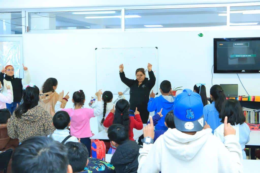 Aprendizaje en aula con maestra y estudiantes participando en actividad interactiva en un salón de clases moderno.