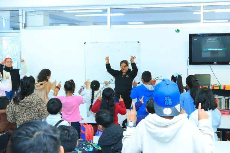 Aprendizaje en aula con maestra y estudiantes participando en actividad interactiva en un salón de clases moderno.