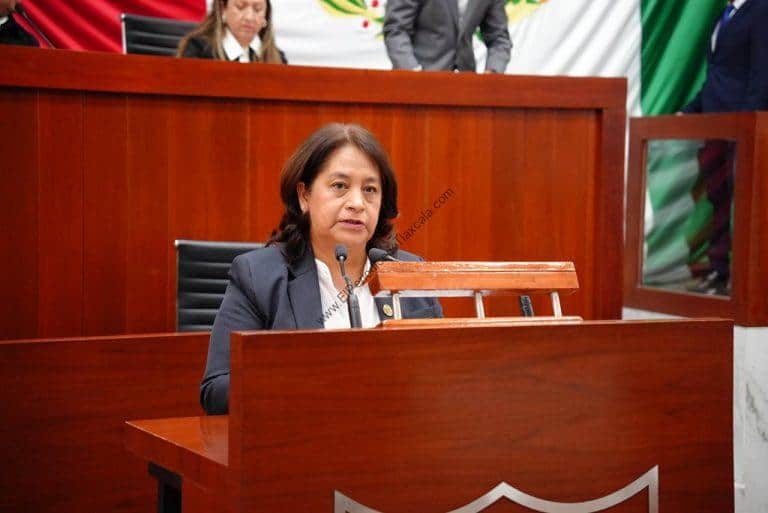 Mujer en un juicio o audiencia en un entorno formal, sentada en un escritorio de madera con micrófono, en un ambiente oficial y profesional.