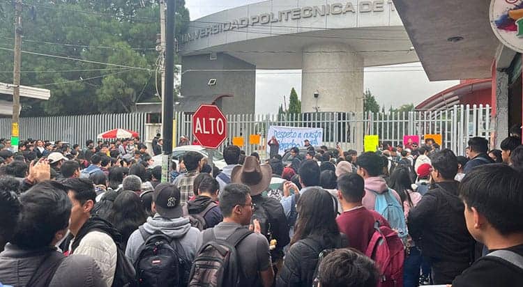 Estudiantes y personas protestan frente a la entrada de la universidad, con carteles y una gran multitud en un día nublado en Tlaxcala, México.