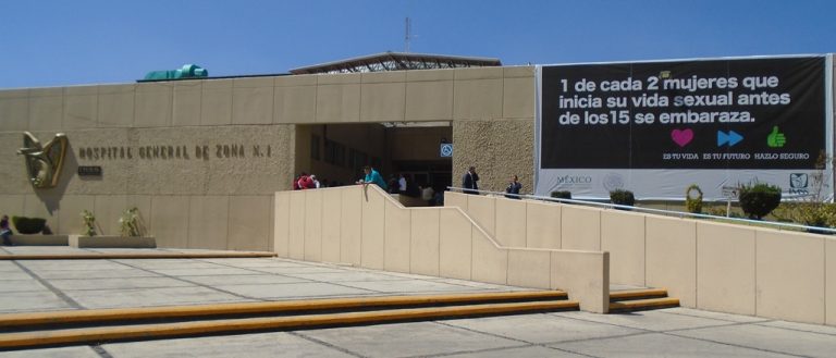 Paciente en la entrada del Hospital General de Zumpango, con cartel informativo sobre la prevención del embarazo en adolescentes y la salud reproductiva.