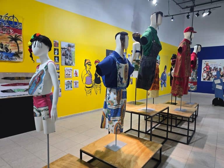 Vestido tradicional mexicano en exhibición en un museo, con fondo amarillo y paredes decoradas con arte y fotografías relacionadas con la cultura de Tlaxcala.