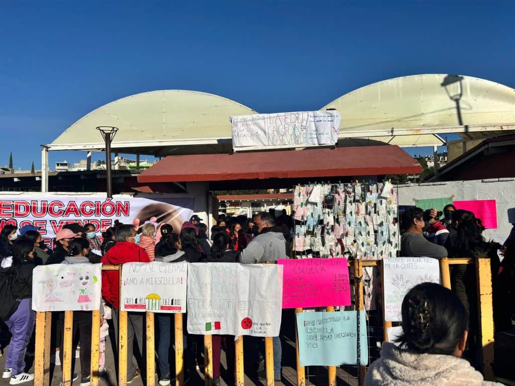 Protesta estudiantil en Tlaxcala con carteles y pancartas frente a un edificio escolar, en un día soleado.