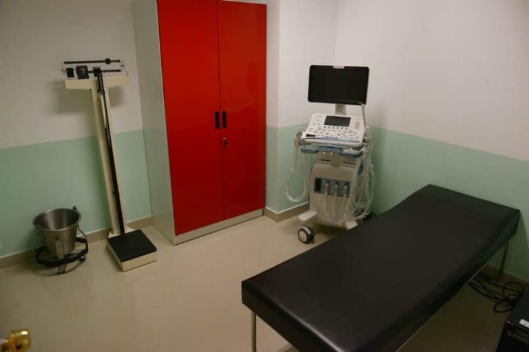Sala de examen médico con camilla, equipo de diagnóstico y armario rojo en una clínica de Tlaxcala, México.