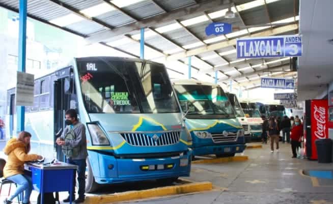 Autobuses en la terminal de Tlaxcala, esperando a los pasajeros para su próximo destino en la ciudad y el estado. Personas comprando boletos y esperando en un ambiente moderno y organizado.