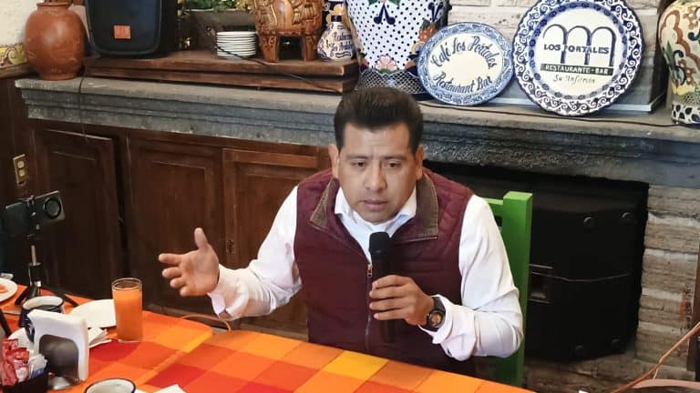 Persona hablando en una entrevista o conferencia, sosteniendo un micrófono en un ambiente interior con decoración tradicional y cerámicas en el fondo.