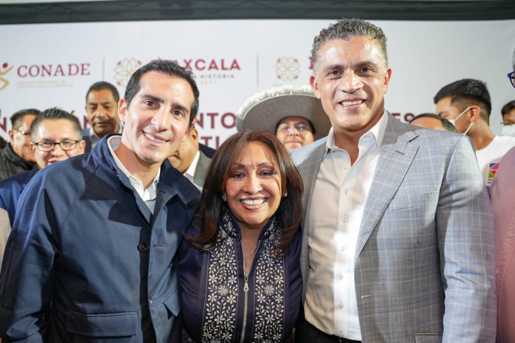 Grupo de personas sonriendo en un evento oficial, con fondo de logotipos de instituciones y autoridades, en un ambiente formal y de celebración.