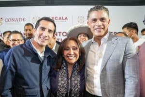 Grupo de personas sonriendo en un evento oficial, con fondo de logotipos de instituciones y autoridades, en un ambiente formal y de celebración.