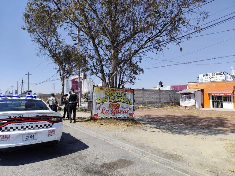 Policía y autoridades en la escena de un incidente en Tlaxcala, con un cartel que anuncia un mole de guajolote en un puesto local.