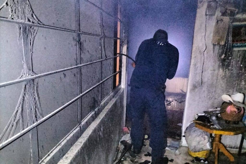 Persona en un ambiente oscuro y dañado, con paredes afectadas y cables expuestos, en un espacio que parece ser un lugar en condiciones precarias.