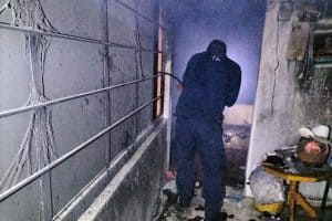 Persona en un ambiente oscuro y dañado, con paredes afectadas y cables expuestos, en un espacio que parece ser un lugar en condiciones precarias.