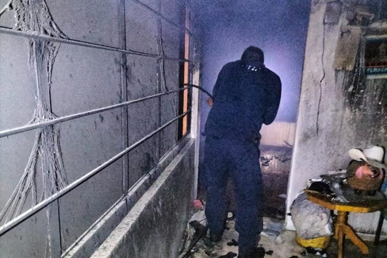 Persona en un ambiente oscuro y dañado, con paredes afectadas y cables expuestos, en un espacio que parece ser un lugar en condiciones precarias.