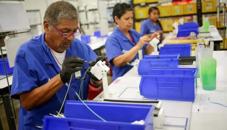 Trabajadores en una línea de ensamblaje en una fábrica, manipulando componentes electrónicos con atención y precisión.