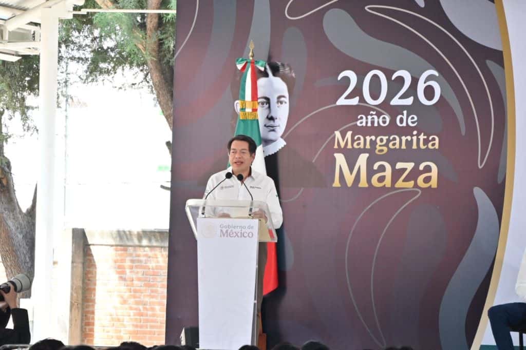 Persona hablando en un evento oficial con fondo que dice "2026 año de Margarita Maza" y bandera de México, en un entorno al aire libre.