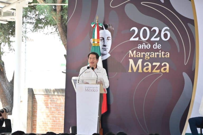 Persona hablando en un evento oficial con fondo que dice "2026 año de Margarita Maza" y bandera de México, en un entorno al aire libre.