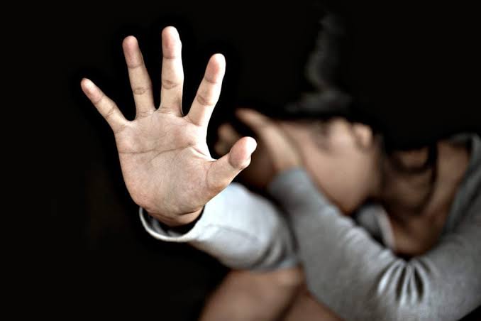 Persona con mano extendida en señal de rechazo, en primer plano, fondo borroso de una mujer con expresión de angustia y tristeza.