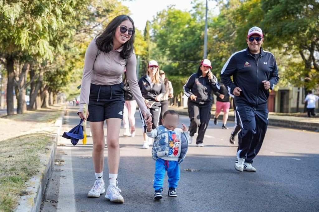 Persona caminando con un niño pequeño en una calle arbolada durante el día, en un ambiente relajado y familiar.