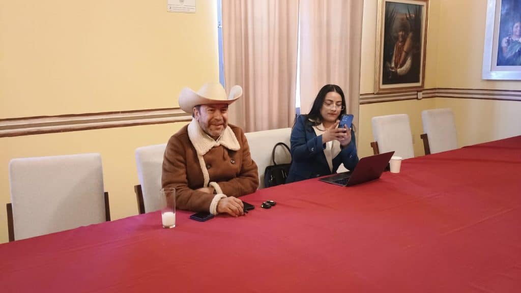 Hombre con sombrero de vaquero y mujer usando teléfono en una sala de reuniones con paredes decoradas.
