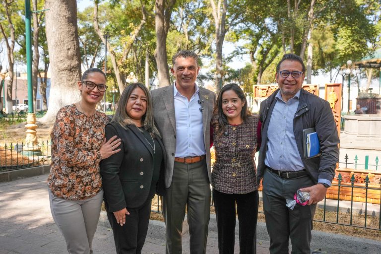 Personas sonriendo y posando juntas en un parque con árboles y juegos infantiles en el fondo.