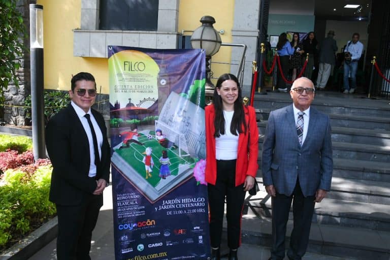 Tres personas en la entrada de un edificio, con un cartel promocional de un evento cultural en Tlaxcala, México.