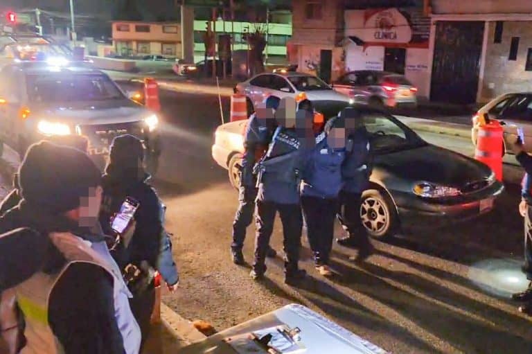 Policías en escena de un accidente vial en una calle de Tlaxcala durante la noche, con vehículos detenidos y señalización de advertencia en el lugar.