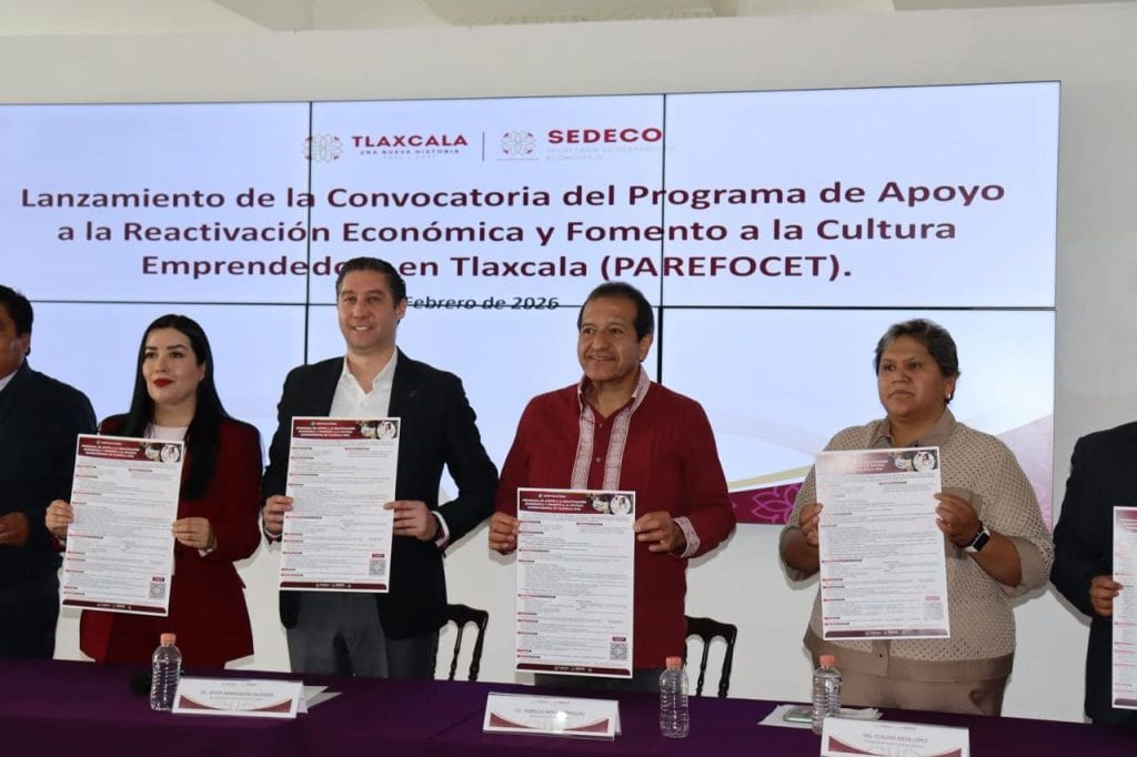 Cuatro personas sosteniendo documentos durante el lanzamiento de la convocatoria del programa de apoyo en Tlaxcala, en un evento oficial con pantalla de fondo.