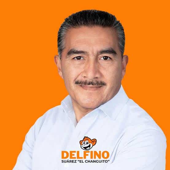Hombre con bigote y cabello peinado hacia atrás, vistiendo una camisa blanca, en fondo naranja.