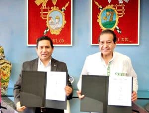 Conferencia de dos hombres en una oficina, sosteniendo documentos en carpetas negras, con escudos y arte en el fondo.