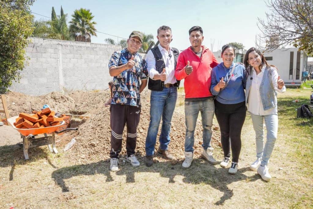 Jóvenes participando en un proyecto de construcción en un espacio al aire libre en Tlaxcala, México, con herramientas y materiales de construcción visibles en el fondo.