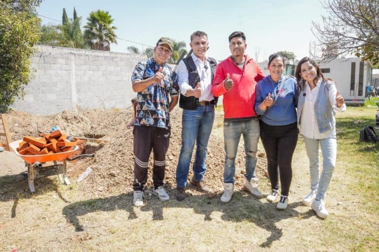 Jóvenes participando en un proyecto de construcción en un espacio al aire libre en Tlaxcala, México, con herramientas y materiales de construcción visibles en el fondo.