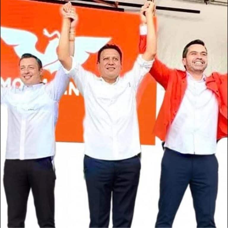 Candidatos políticos celebrando con las manos levantadas en un evento de campaña en Tlaxcala, con fondo naranja y logotipo del partido.