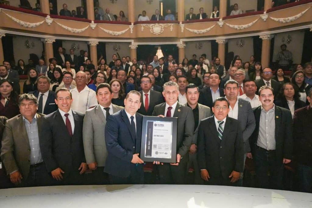 Reconocimiento oficial en un evento formal con un grupo de personas vestidas con trajes elegantes en un teatro o auditorio.