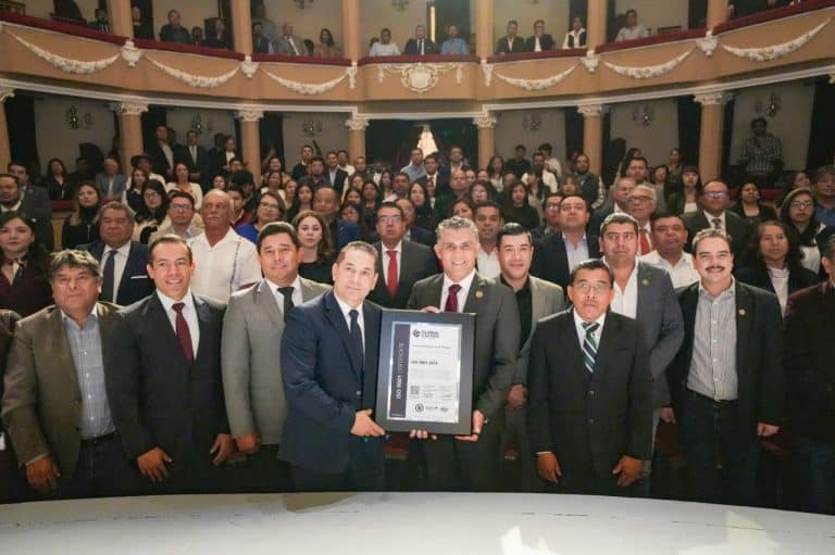 Reconocimiento oficial en un evento formal con un grupo de personas vestidas con trajes elegantes en un teatro o auditorio.