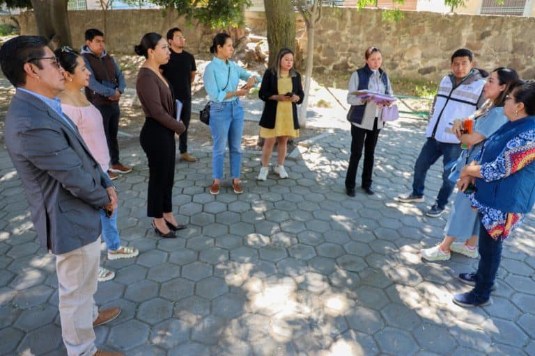 Grupo de personas en una reunión al aire libre, participando en una actividad de discusión o presentación en un espacio con árboles y piso de adoquines.